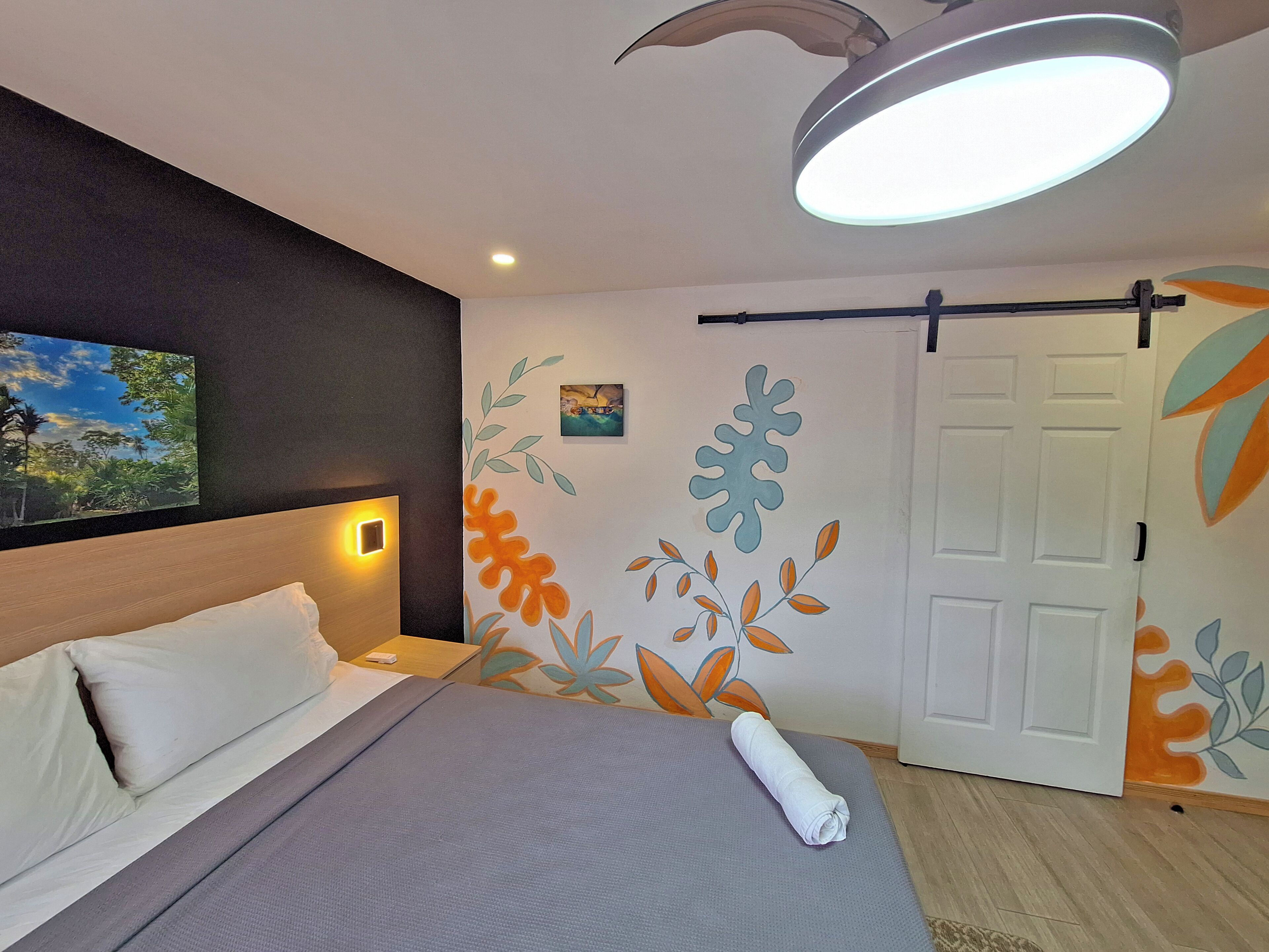 A hotel room with a bed, a wall-mounted light, a painting, and a door.