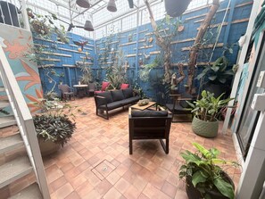 A cozy indoor garden with a black sofa, chairs, and various potted plants. - Jungla Urbana BnB - Adults Only (San José)