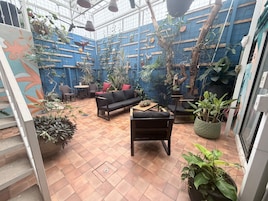 Un jardín interior acogedor con un sofá negro, sillas y diversas plantas en macetas.