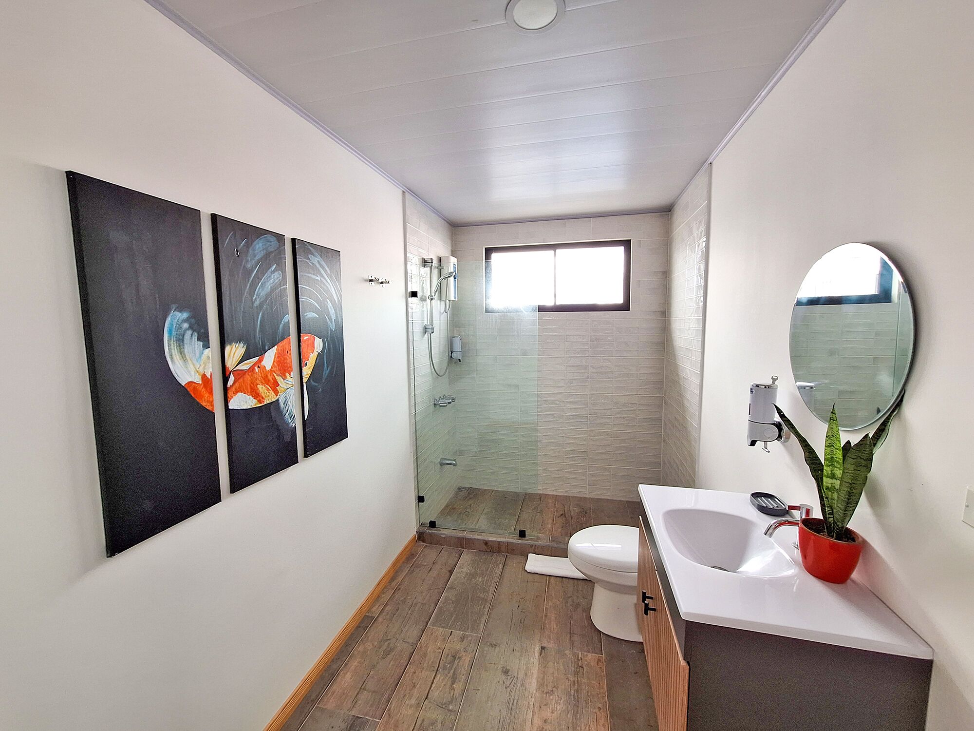 A modern bathroom with a wooden floor, a white sink, a mirror, and a toilet.