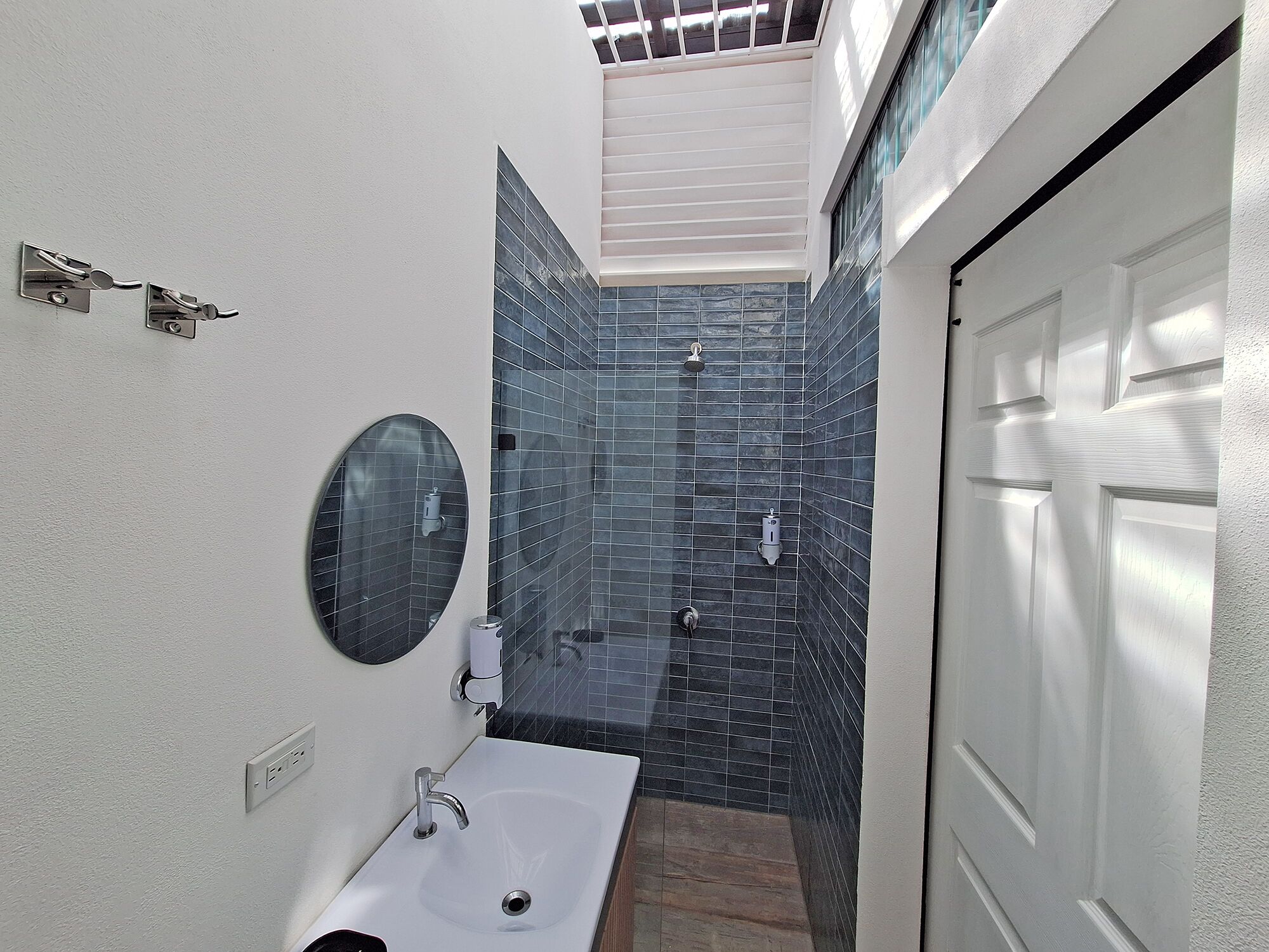 A bathroom with a white sink, a mirror, a shower with dark blue tiles, and a white door.