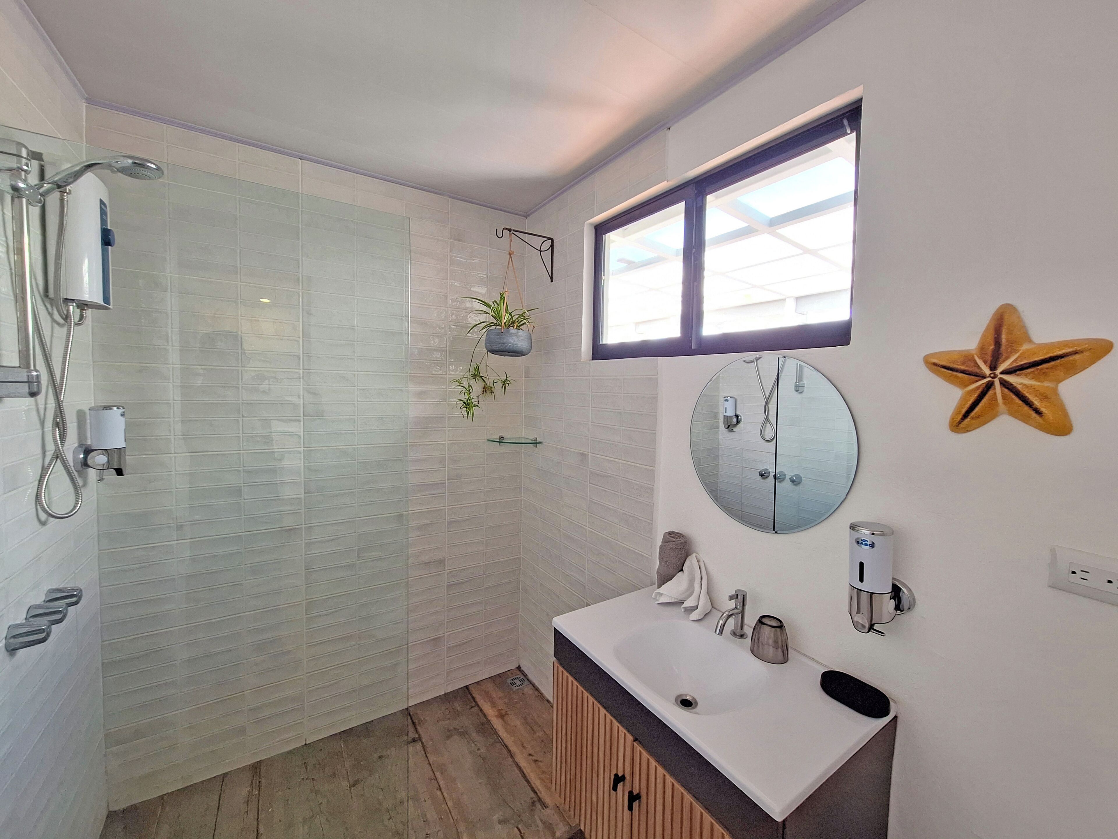 Bany modern amb boxa de dutxa de vidre, un lavabo amb mirall i una decoració de estrella de mar a la paret.