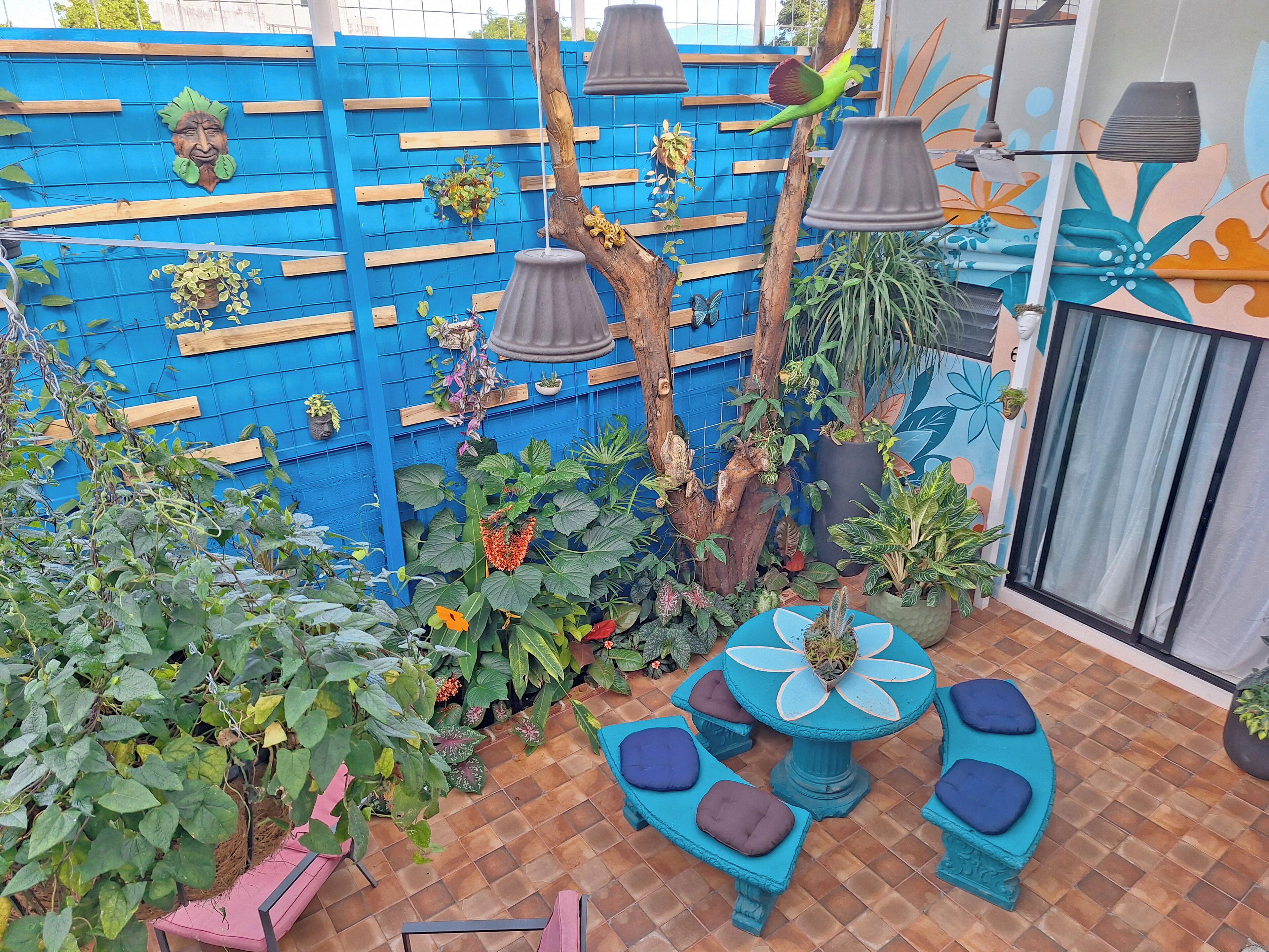 A patio area with a blue fence, various potted plants, a birdcage, and a blue table with cushioned seats.