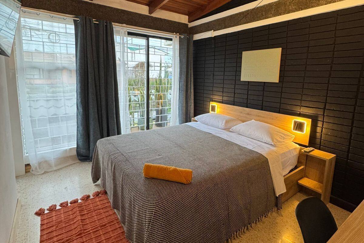 Un dormitorio con cama, ventilador de techo, mesita de noche y ventana con cortinas.
