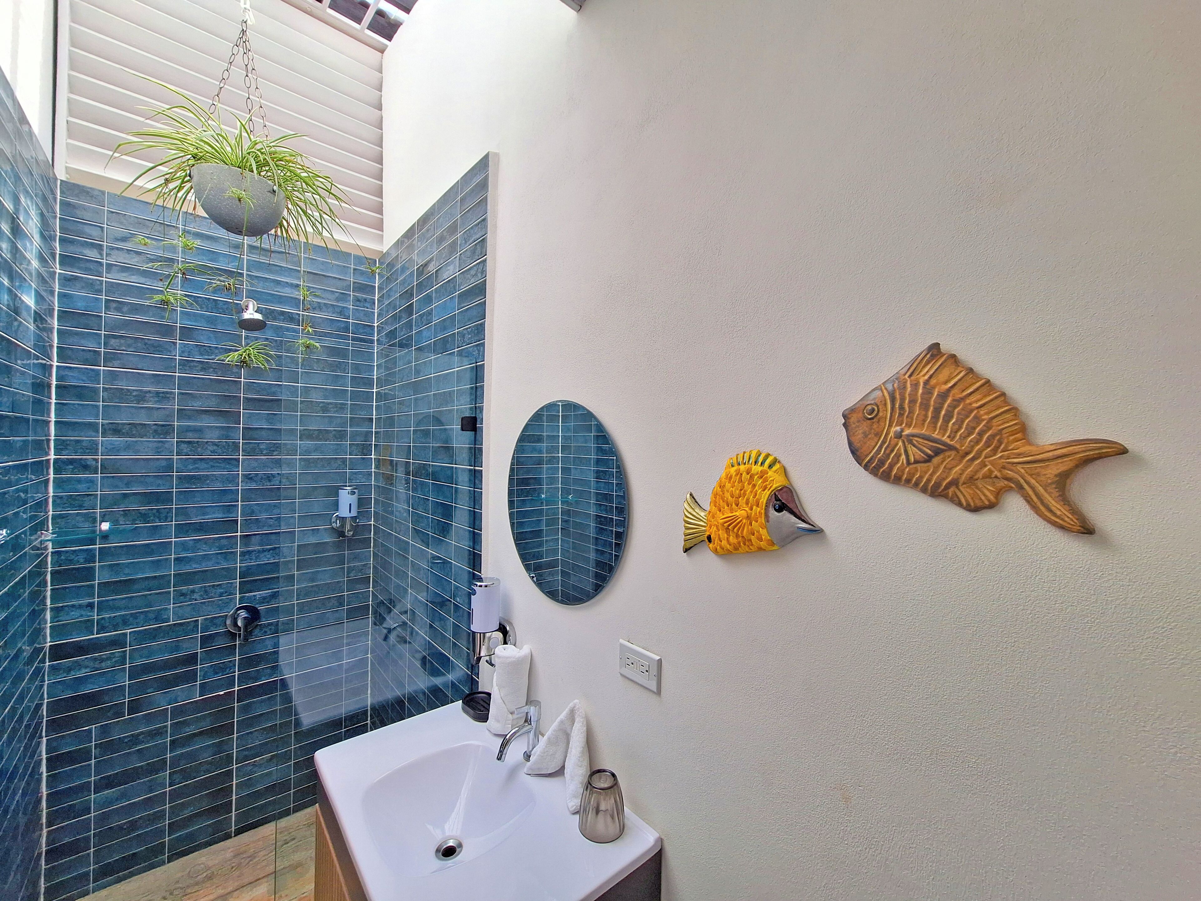 Een badkamer met een blauw betegelde douche, een witte wastafel en decoratieve vissen aan de muur.