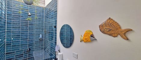 Een badkamer met een blauw betegelde douche, een witte wastafel en decoratieve vissen aan de muur.