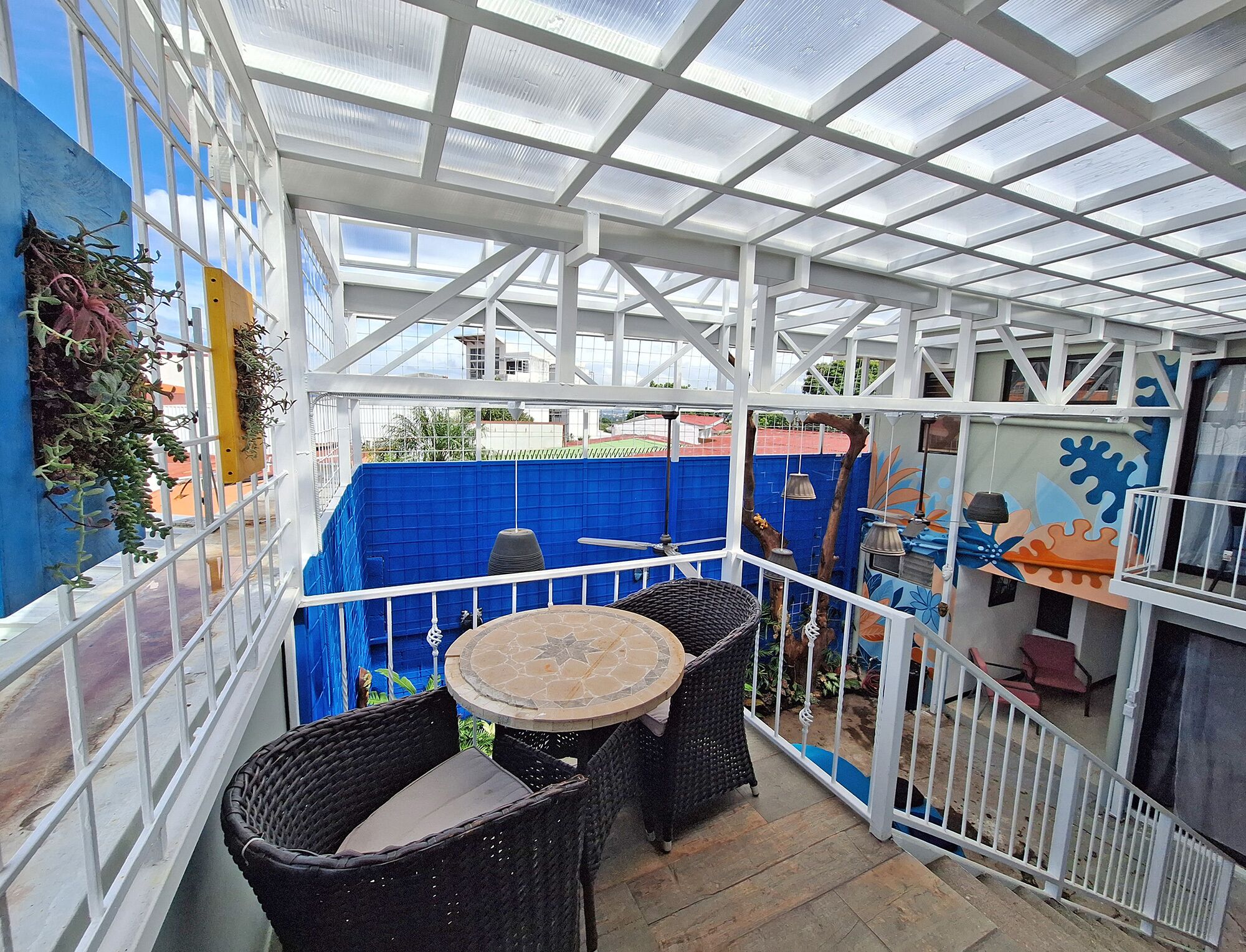 A covered patio area with a glass ceiling, wicker furniture, and a blue wall with plants.