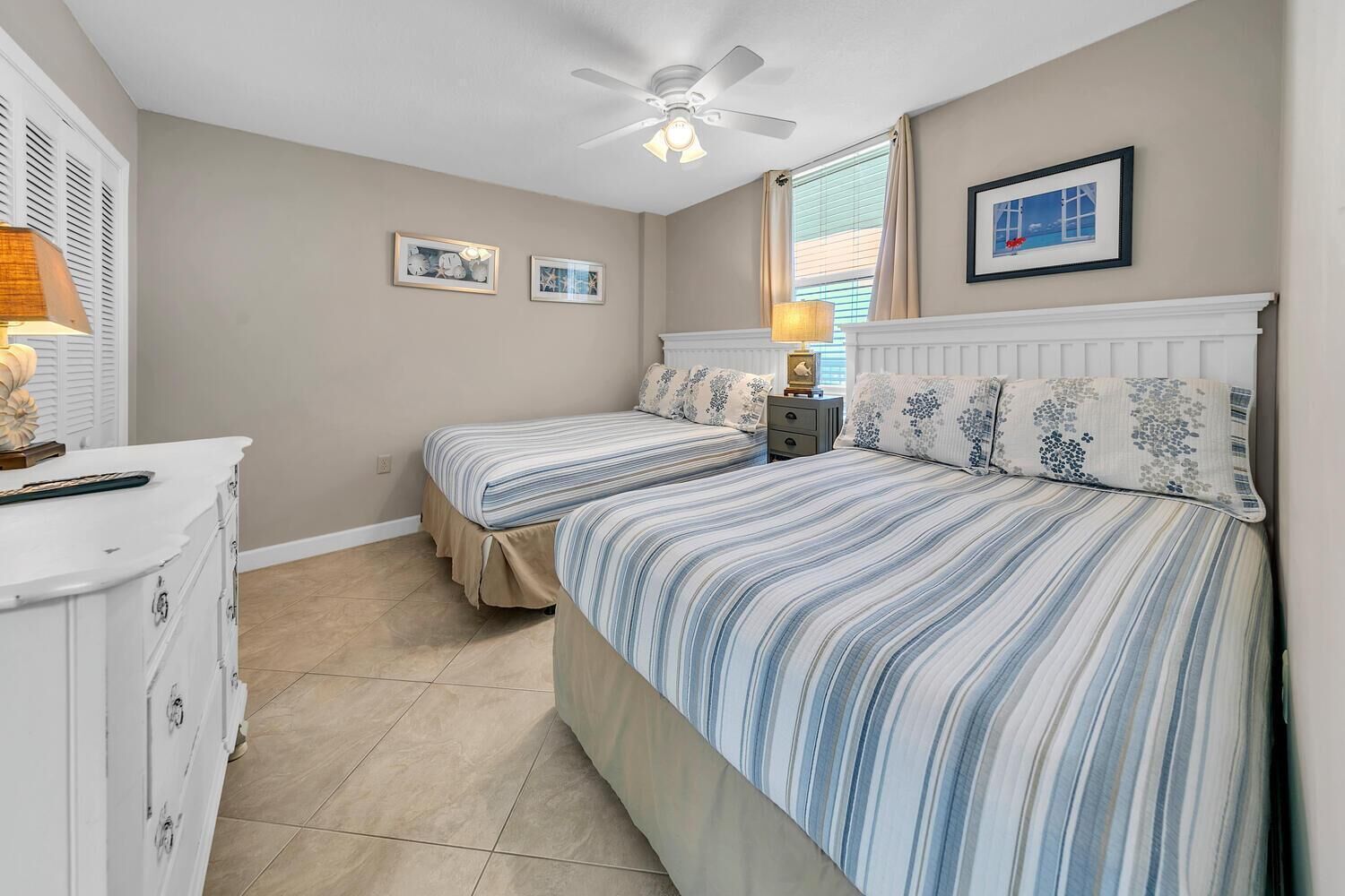 A bedroom with two beds, a dresser, a ceiling fan, and a window with curtains.