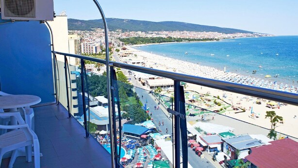 A balcony with a view of a beach, a table, and chairs. - Hotel Palace (Nessebar)