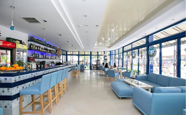 A modern bar area with a long counter, blue seating, and large windows.