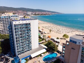 A high-rise hotel with a pool and beach view, multiple balconies, and a clear blue sea.