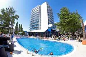 A hotel with a pool, outdoor seating, and a tall building with balconies.