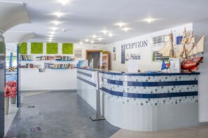 A reception area with a tiled counter, a wall-mounted clock, and a display of sailing ships. - Hotel Palace (Nessebar)