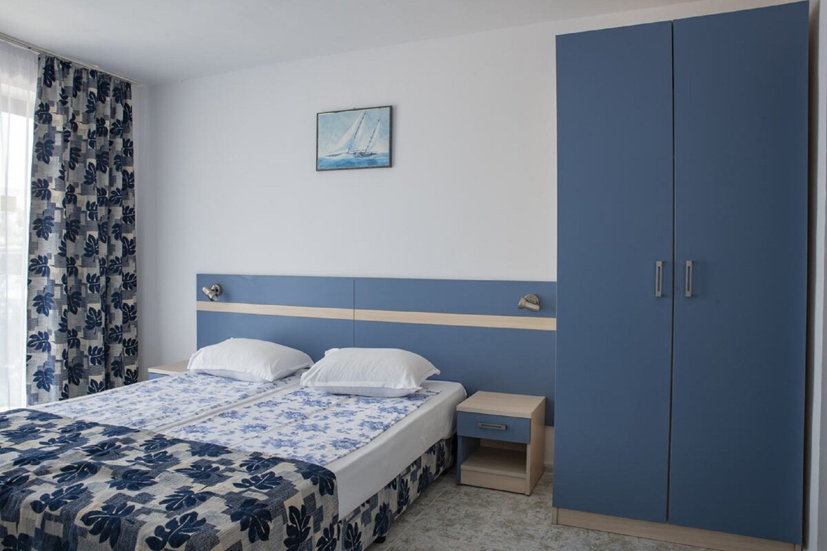 A bedroom with a bed, nightstand, wardrobe, and a sailboat painting on the wall.