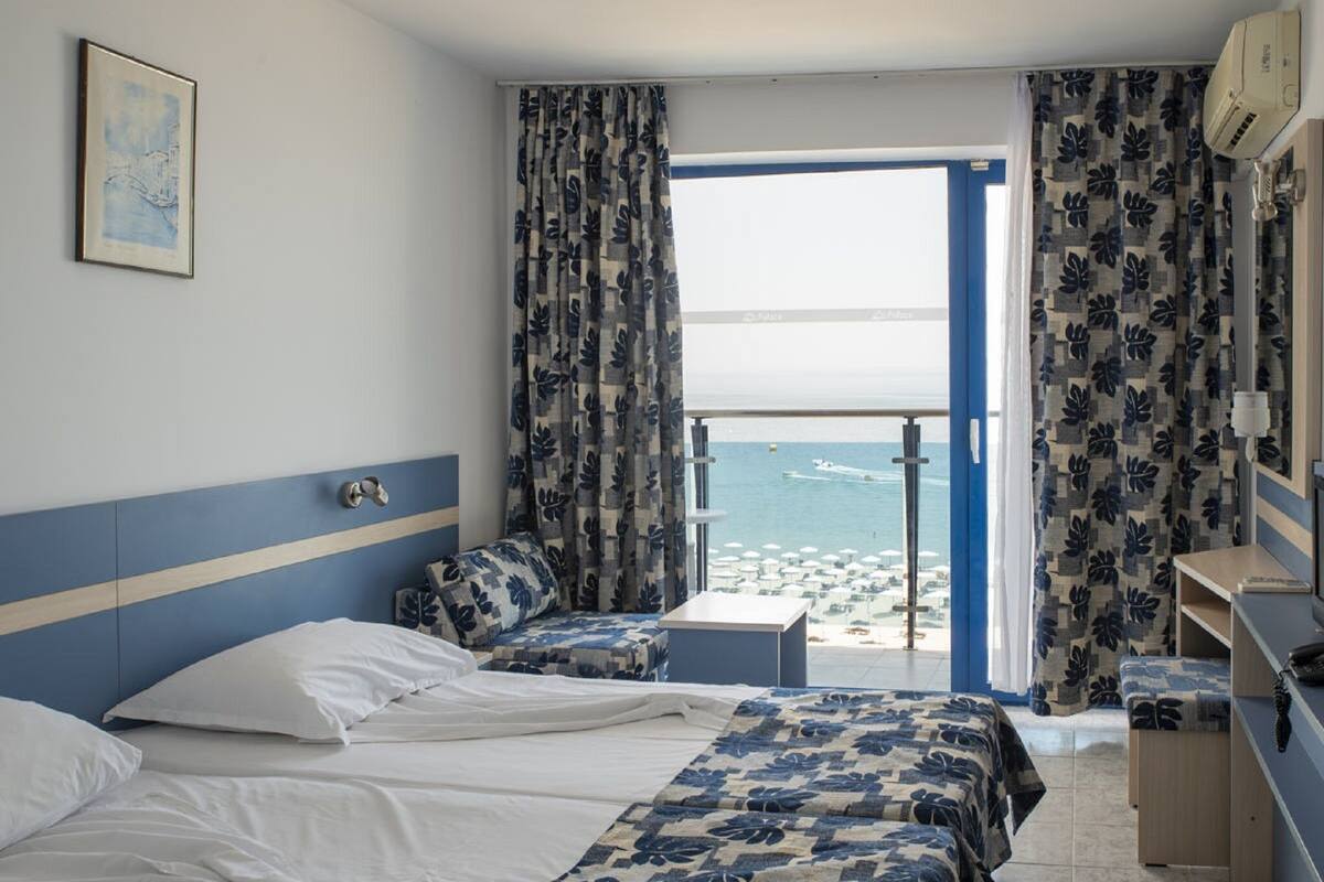 Ein Hotelzimmer mit Bett, Sitzecke, kleinem Tisch und Blick auf Strand und Meer.