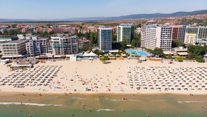 An aerial view of a coastal area with a beach, multiple hotel buildings, and a clear sky. - Hotel Palace (Nessebar)