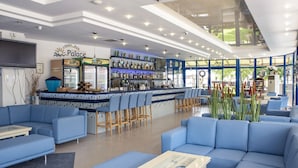 A modern lobby with blue seating, a bar area, and a large window offering a view of the outdoors. - Hotel Palace (Nessebar)