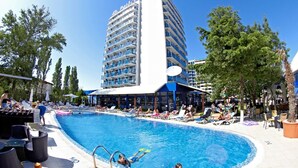 A hotel with a pool, outdoor seating, and a tall building with balconies. - Hotel Palace (Nessebar)