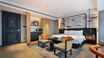 A hotel room with a bed, two armchairs, a small table, and a kitchenette.