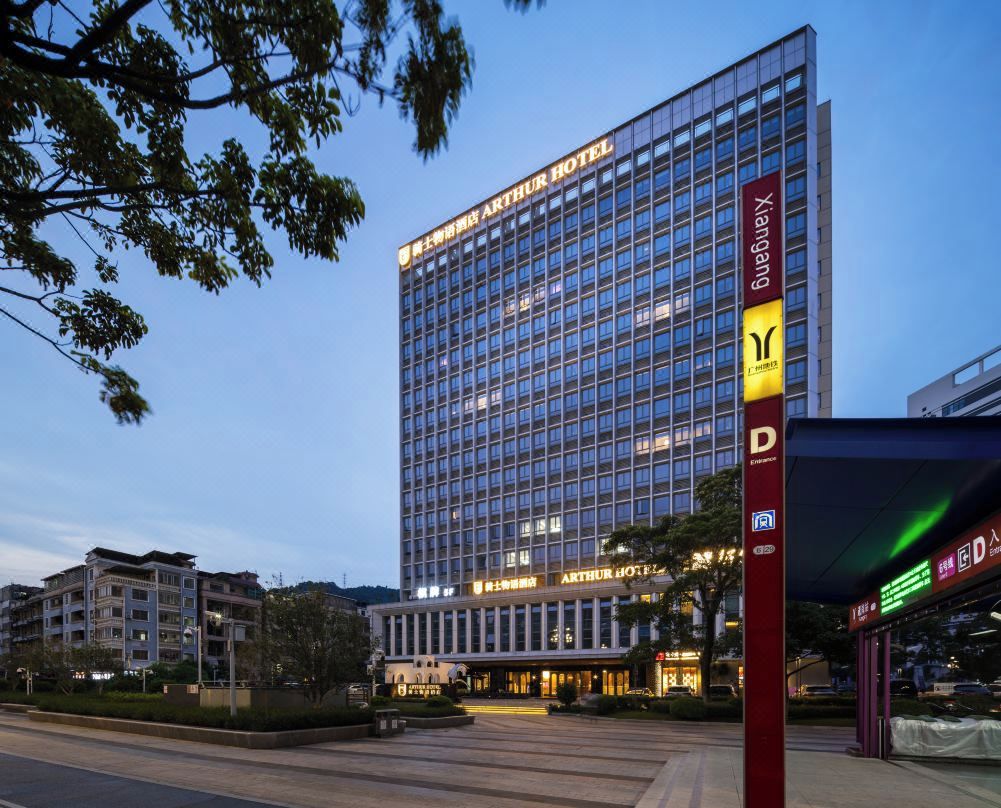 A modern Arthur Hotel with a large glass facade, a prominent entrance, and a red pillar with signage.