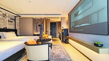 A modern hotel room with a large bed, a seating area with a table, a television mounted on the wall, and a small plant on a shelf.