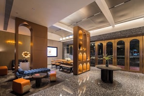 A modern hotel lobby with seating arrangements, a reception desk, and a large screen displaying the hotel name. - Arthur Hotel (Guangzhou)