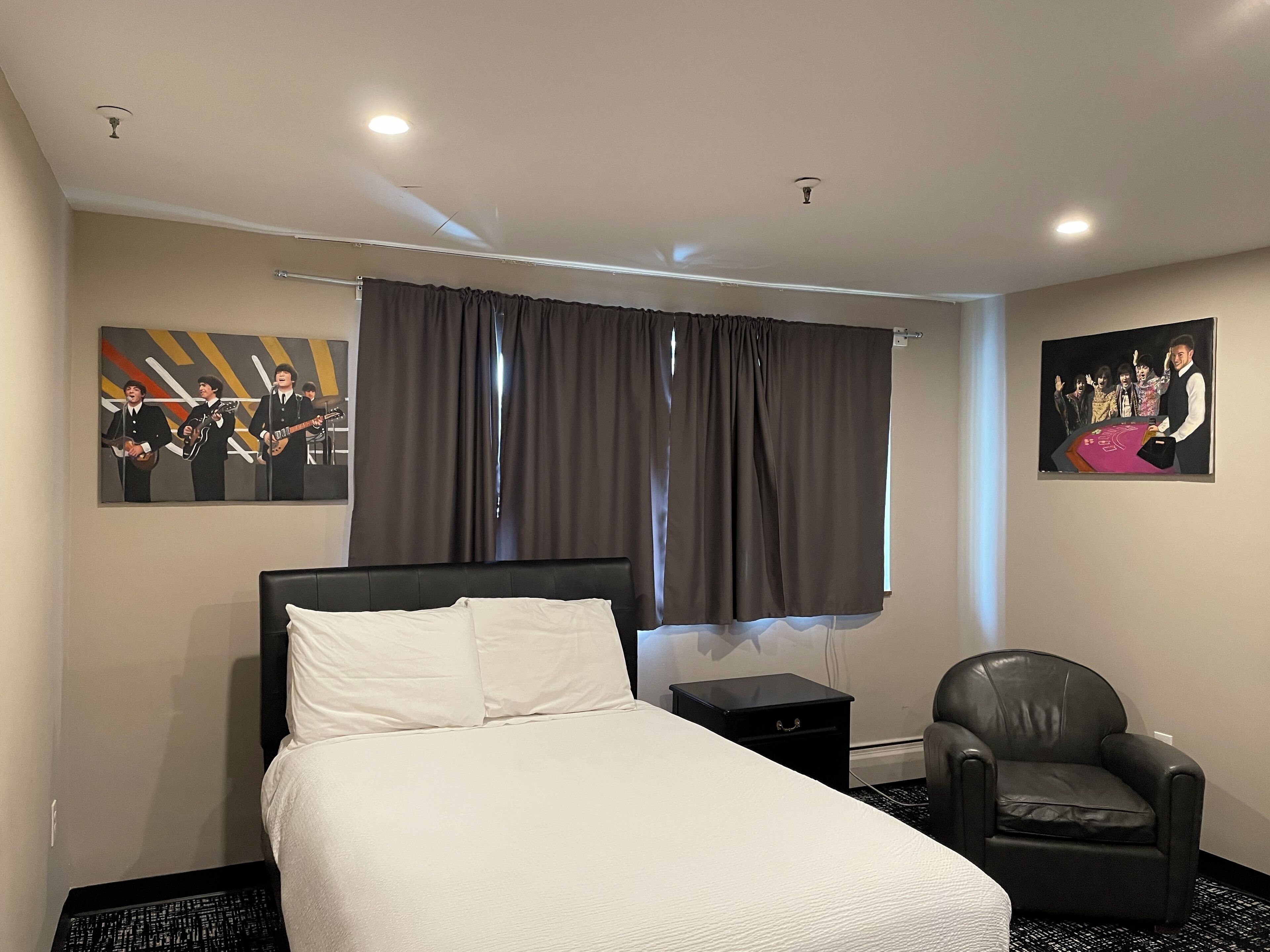 A hotel room with a bed, a chair, a nightstand, and two wall art pieces.