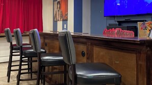 Angolo bar con schermo piatto, bancone in legno e quattro sgabelli in pelle.