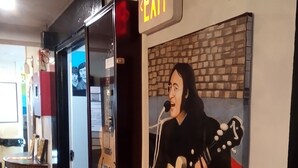 Un muro con una figura che suona la chitarra, una segnaletica di uscita e una porta in vetro.