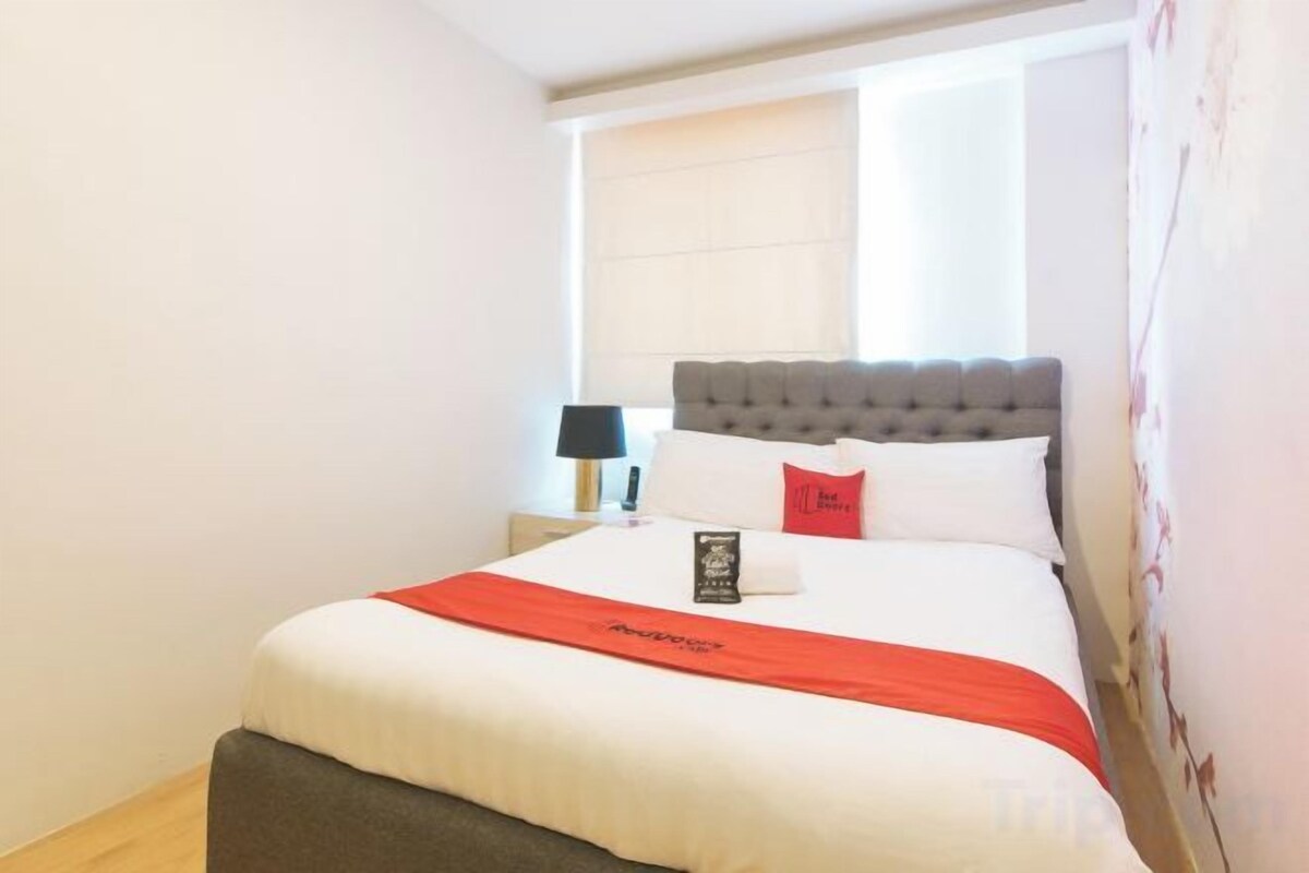 A hotel room with a bed, a nightstand, a lamp, and a window with curtains.