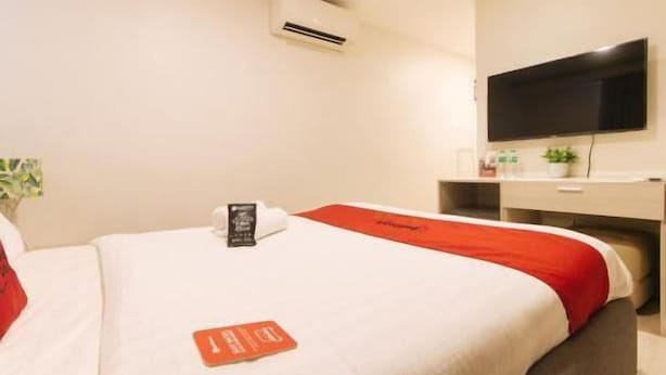 Una camera d'albergo con due letti, una scrivania, una TV a schermo piatto e una piccola pianta.
