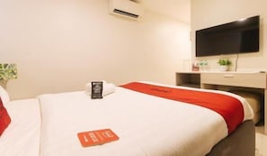 Ein Hotelzimmer mit zwei Betten, einem Schreibtisch, einem Flachbildfernseher und einer kleinen Pflanze.