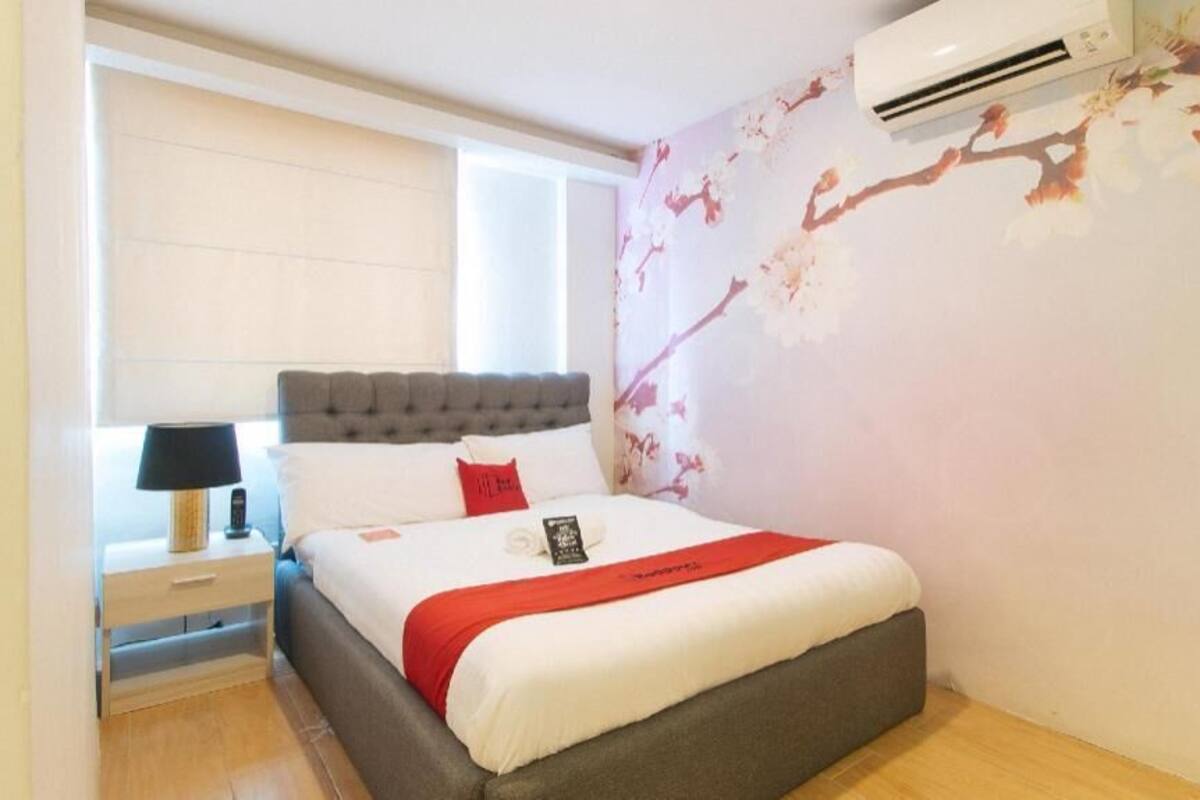 Une chambre à coucher comprenant un lit, une table de chevet, une lampe, un climatiseur fixé au mur et une fenêtre.