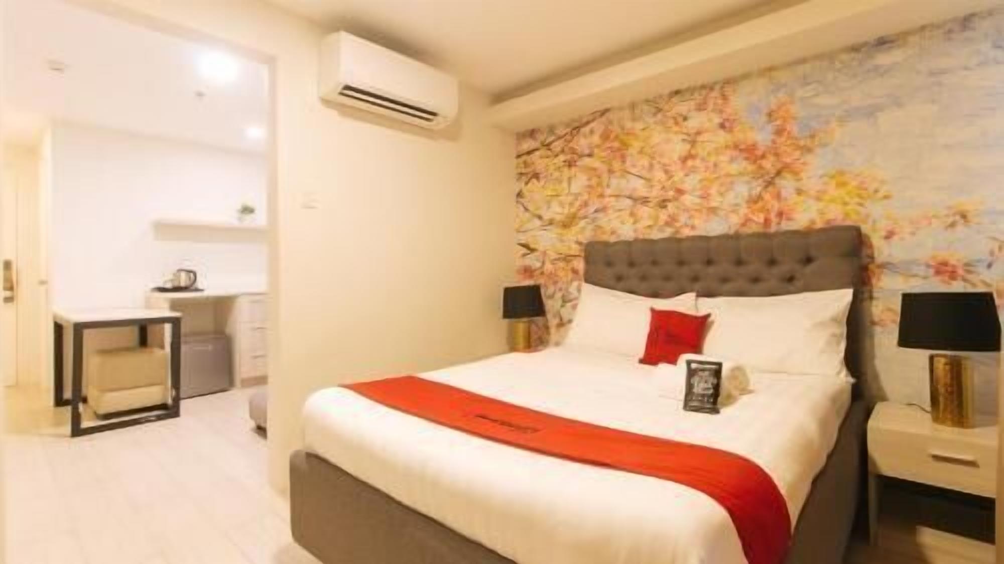 A hotel room with a bed, a nightstand, a bedside table, an air conditioning unit, and a bathroom visible in the background.