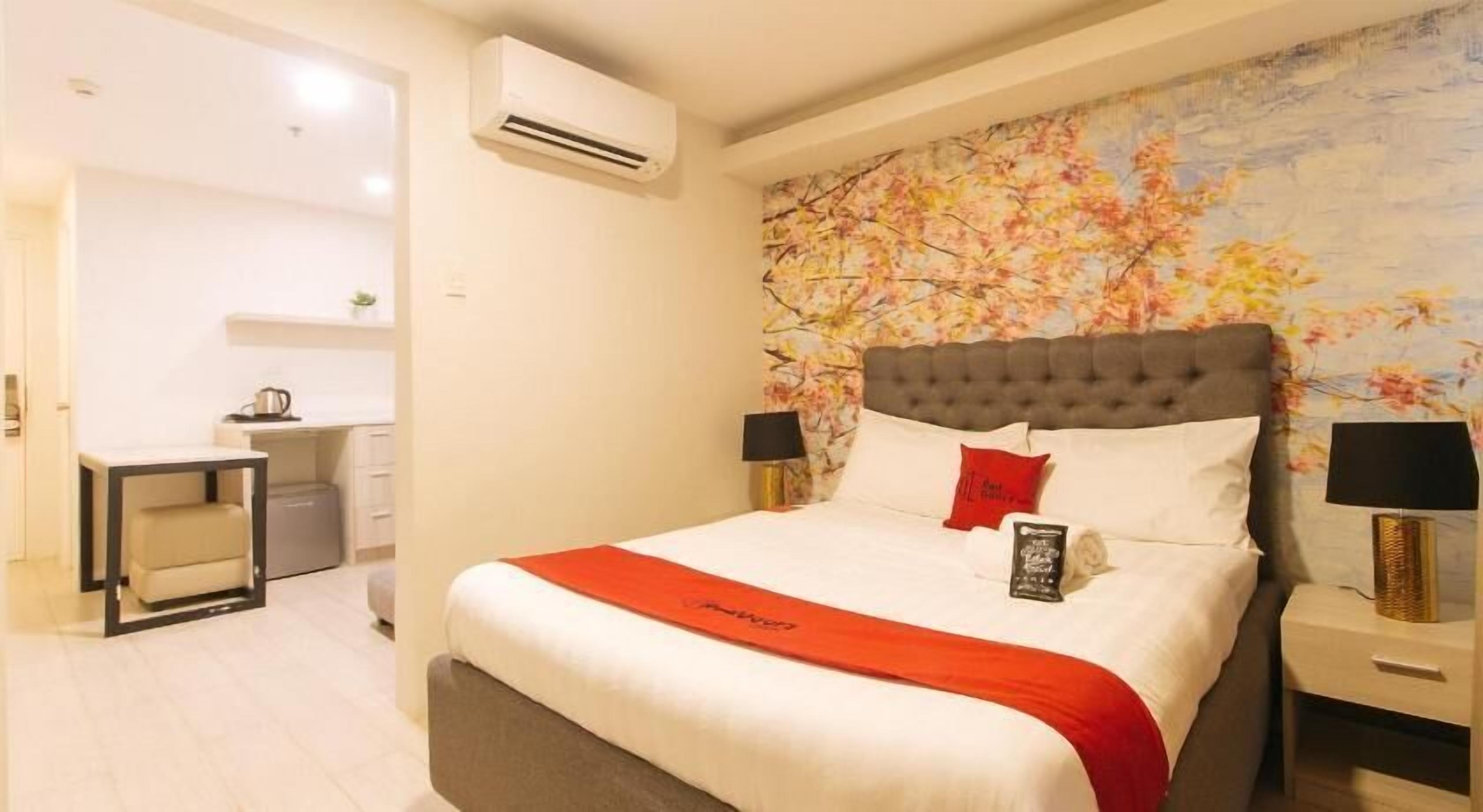 A hotel room with a bed, a desk, and an air conditioning unit.