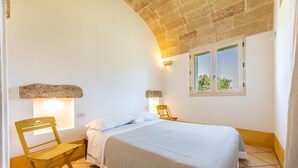 A bedroom with a bed, a wooden chair, a stone shelf, and a window with a view of greenery. - Appartamento Cappero - Torre Vado (Torre vado)