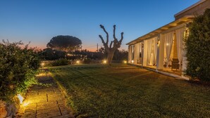A well-lit outdoor area with a stone pathway leading to a building with large windows and a covered patio area. - Appartamento Cappero - Torre Vado (Torre vado)