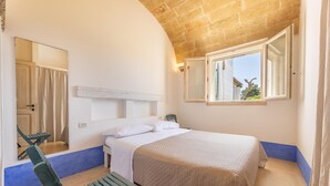 A bedroom with a bed, a chair, a window, and a mirror.
