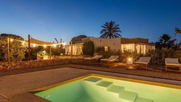 A swimming pool with steps, lounge chairs, and string lights at dusk.