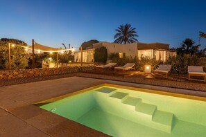 Ein Pool mit Stufen, Liegestühlen und Lichterketten im Dämmerlicht.