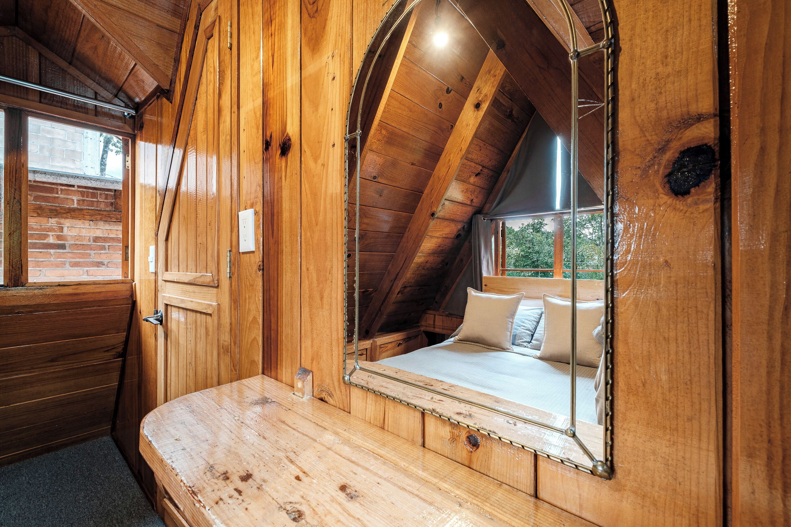 A wooden interior with a sloped ceiling, a bed with pillows, and a large mirror.