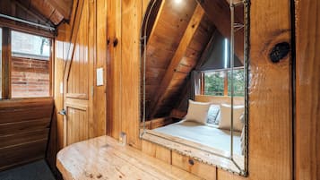 A wooden interior with a sloped ceiling, a bed with pillows, and a large mirror.