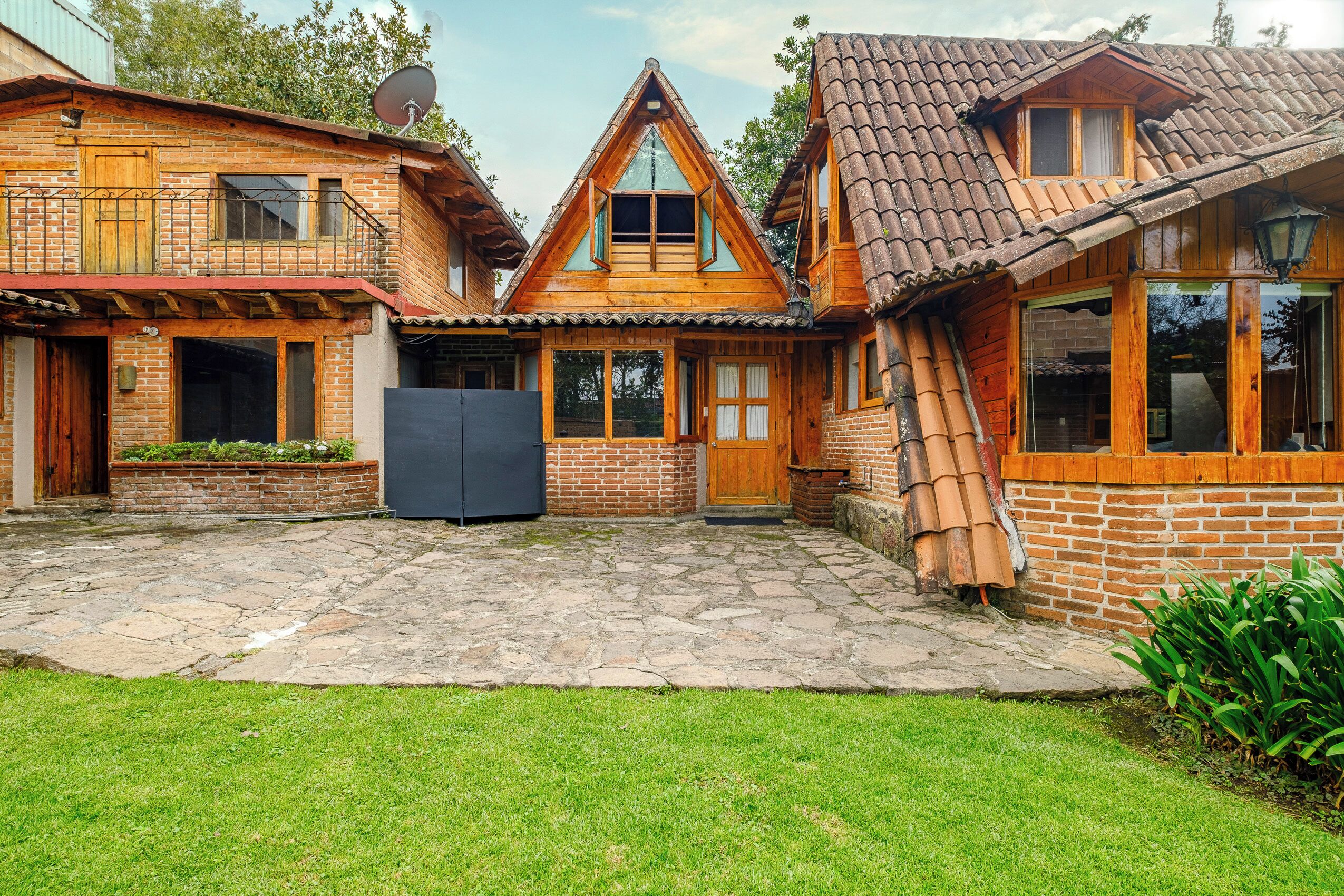 A wooden house with a stone patio, a wooden door, and a satellite dish.