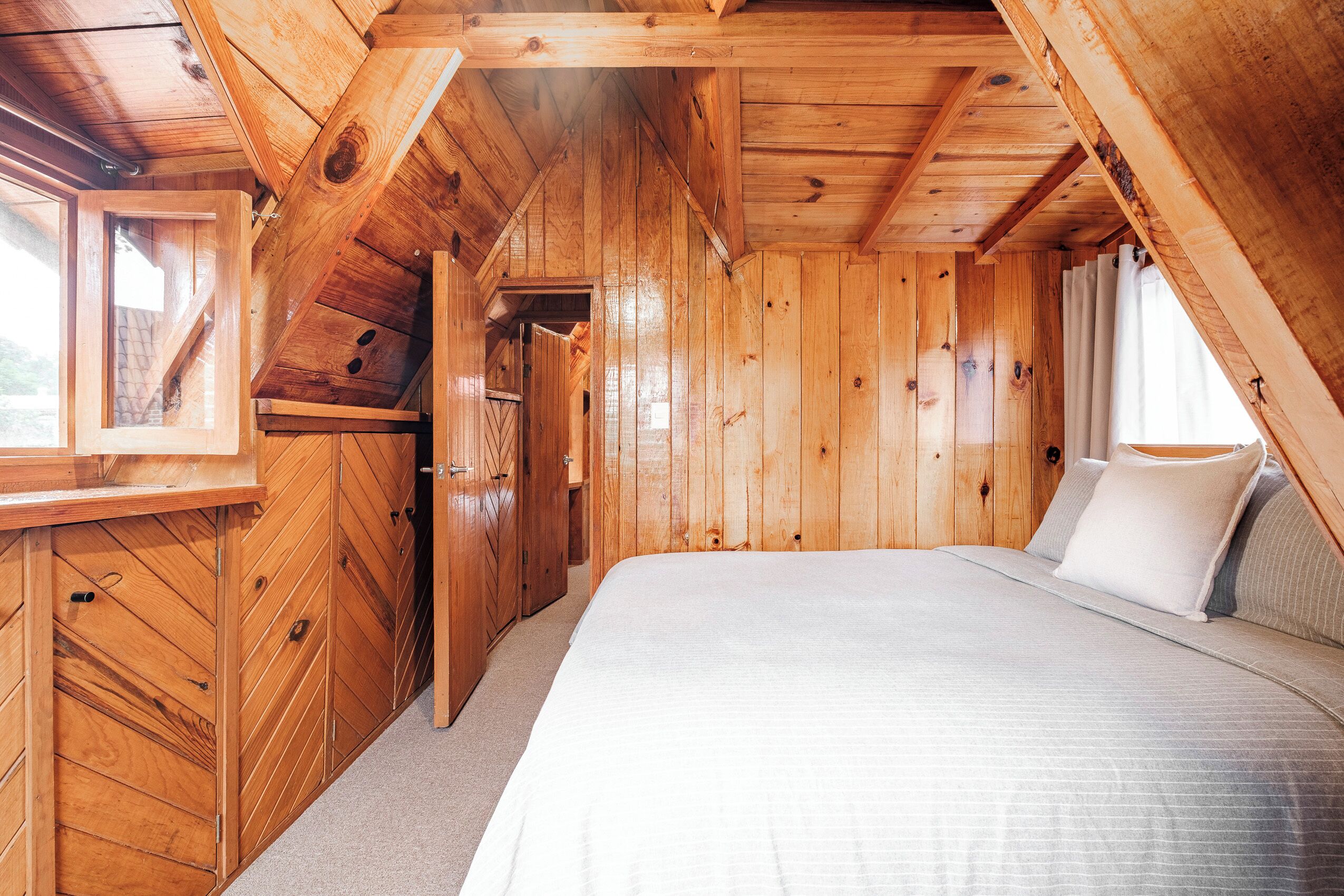 A wooden cabin bedroom with a bed, a window, and a door.