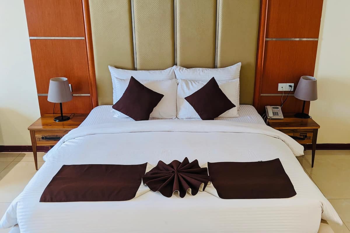 A hotel room with a large bed, two bedside tables, a telephone, and a wall-mounted light fixture.
