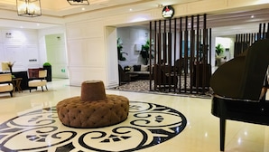 A lobby with a tufted ottoman, a grand piano, and a decorative floor pattern.