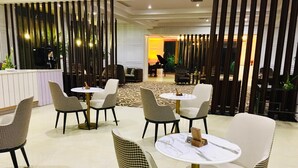 A modern hotel lobby with checkered chairs and round tables, a reception desk, and a patterned carpet.