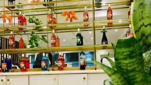 A bar area with shelves displaying various bottles, a counter, and a potted plant.