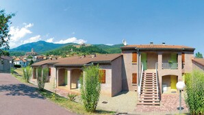Een rij traditionele gebouwen in mediterrane stijl met terracottadaken, een centrale trap en een berg op de achtergrond.