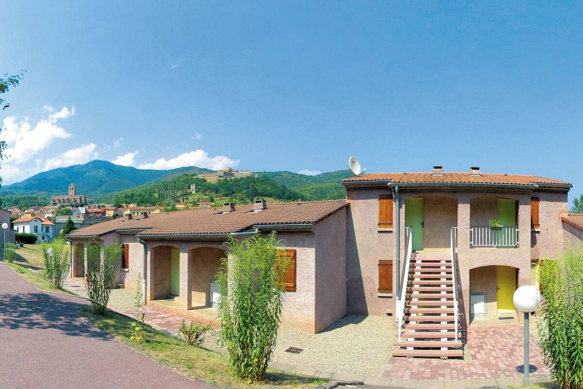 Een rij traditionele gebouwen in mediterrane stijl met terracottadaken, een centrale trap en een berg op de achtergrond.